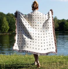 a woman is holding up a blanket with letters on it in front of a body of water