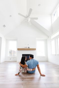 a man and woman sitting on the floor in front of a fire place with their arms around each other