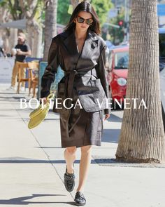 a woman is walking down the street in a trench coat