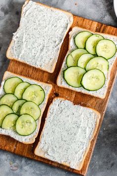 four slices of bread topped with cucumbers and cream cheese on a cutting board