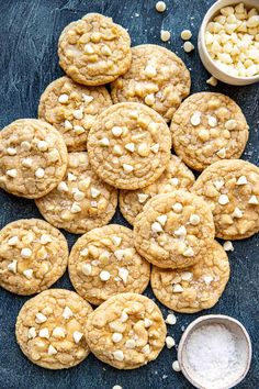 cookies with white chocolate chips and marshmallows on a blue surface next to a bowl of powdered sugar