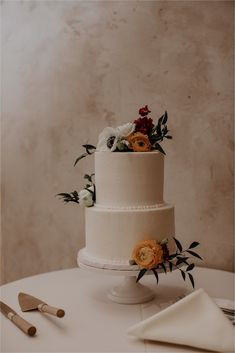 a three tiered cake with flowers on the top is sitting on a table next to utensils