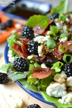 a salad with blackberries and bacon is on a blue plate, ready to be eaten