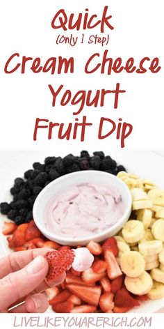 a hand dipping some fruit into a bowl with cream cheese yogurt dip in it