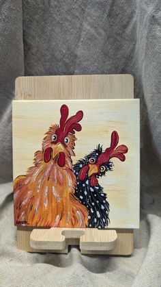 a painting of two roosters on a wood block