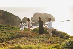 three adults and two children holding hands while standing on a hill overlooking the ocean