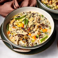 two bowls of chicken and vegetable soup with spoons next to it on a table