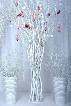 three white vases filled with branches and ornaments