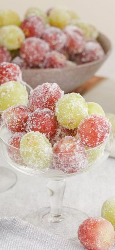 a bowl filled with sugar covered fruit next to another bowl full of grapes on a table