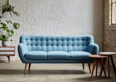 a blue couch sitting in front of a white brick wall next to a wooden table