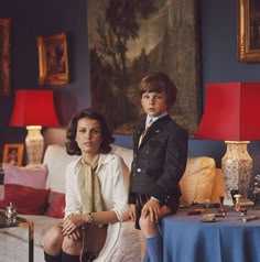 a woman sitting next to a little boy on a couch in front of a painting