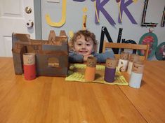 a young child sitting at a table in front of some toilet paper rolls and cardboard boxes