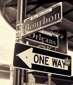 black and white photograph of street signs on the corner of bourbon st and orleans ave