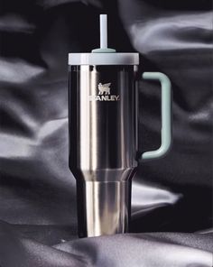 a stainless steel travel mug with a straw in the middle on a black satin background