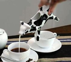 a person pouring milk into a cup with a cow figurine on top of it