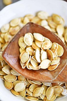 a wooden spoon filled with pumpkin seeds on top of a white plate