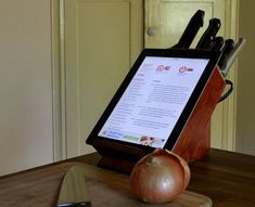 a tablet is sitting on top of a cutting board with knifes and an onion