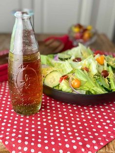 a bottle of apple cider sits next to a salad on a red and white tablecloth