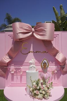 a wedding cake with pink ribbon and flowers on the table in front of a pink backdrop