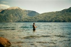 a man wading in the water near mountains