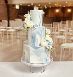 two tiered wedding cake decorated with white and blue flowers on a table in a banquet hall