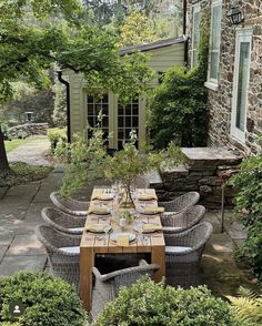 an outdoor dining area with wicker furniture and stone walls, surrounded by greenery