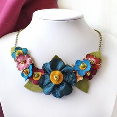 A plush teal blue and plum bib necklace. This bold statement necklace boasts a large teal blue poppy,surrounded by hand cut plum and blue and yellow ochre (or mustard if you prefer) flowers and dotted with plum pansies.  This is a sumptuous addition to my fabric flower jewelry range and is a stunning accessory for a special occasion.SIZE: Entire LENGTH: Choose from four lengths: 46cm (just over 18")51cm (just over 20")56cm (22")61cm (24")The main detail is roughly 18cm (roughly 7") across.The ha Colorful Statement Necklace, Bold Statement Necklaces, Fabric Brooch, Blue Poppy, Bold Necklace, Daisy Necklace, Felt Jewelry, Yellow Daisies, Yellow Ochre