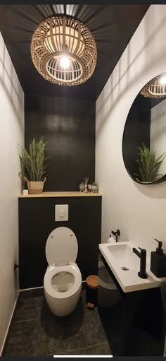 a white toilet sitting next to a bathroom sink under a round light hanging from the ceiling