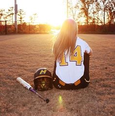 a woman sitting on the ground with a baseball bat and helmet in front of her