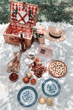 an open picnic basket sitting on top of a blanket next to two plates and food