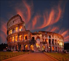 the colossion is lit up at night with pink clouds in the sky above