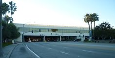 an empty street in front of a building with palm trees on both sides and a traffic light above it