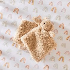 a brown teddy bear laying on top of a white sheet with rainbows in the background