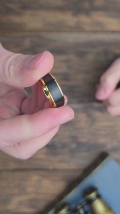 two hands holding an engagement ring on top of a wooden table next to a book