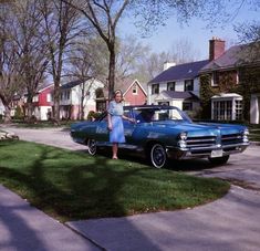 a woman standing next to a blue car in front of a house on a residential street