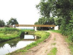 a bridge over a river next to a dirt road and green grass on both sides