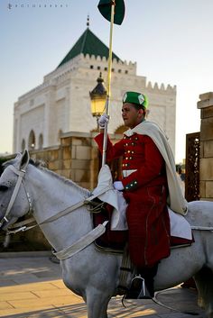 a man dressed in red riding on the back of a white horse with a flag