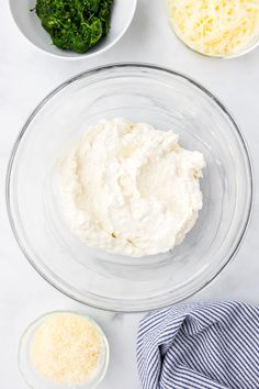 ingredients to make cheese dip in bowls on a white counter top, including parmesan cheese and spinach