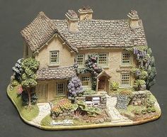 a figurine of a house with flowers and trees on the front lawn, sitting on a black surface