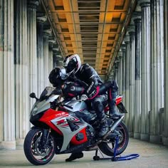 a man riding on the back of a red and silver motorcycle under a wooden bridge