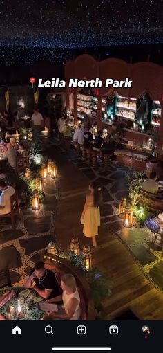 people are sitting at tables in the middle of a night time area with lights on