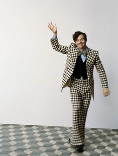 a man in checkered suit and tie walking across a floor with his hand up