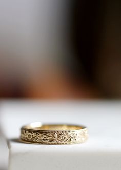 a gold wedding ring sitting on top of a white surface with a blurry background