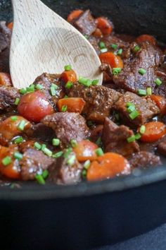 beef and carrots cooking in a skillet with a wooden spoon