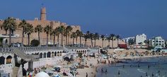 people are on the beach and in the water near an old city with palm trees