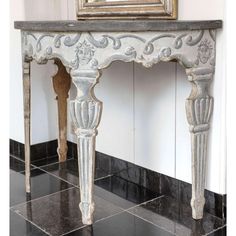 an ornate white console table with black marble flooring in front of a painting on the wall