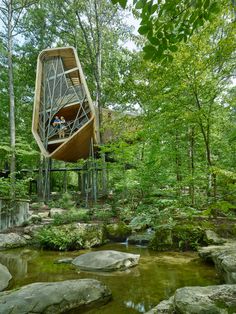 a wooden structure in the middle of a forest filled with rocks and trees, surrounded by water