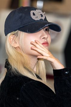 a woman with blonde hair wearing a black hat and looking off to the side while holding her hand near her face