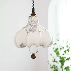 a light fixture hanging from a ceiling in a room with a potted plant behind it