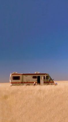 an rv parked in the middle of a dry grass field with blue skies behind it